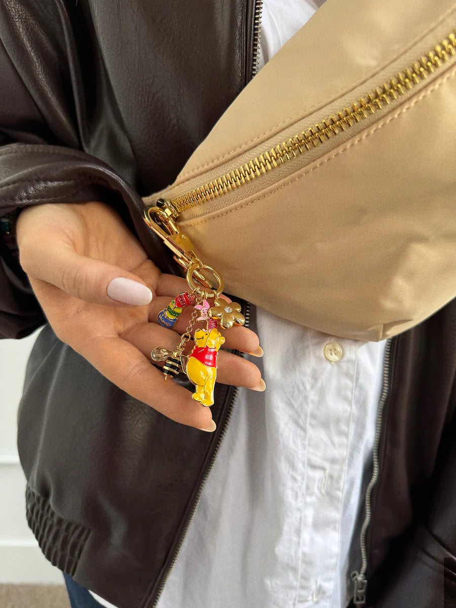 Hand holding a keychain with a bear design in front of a beige bag.