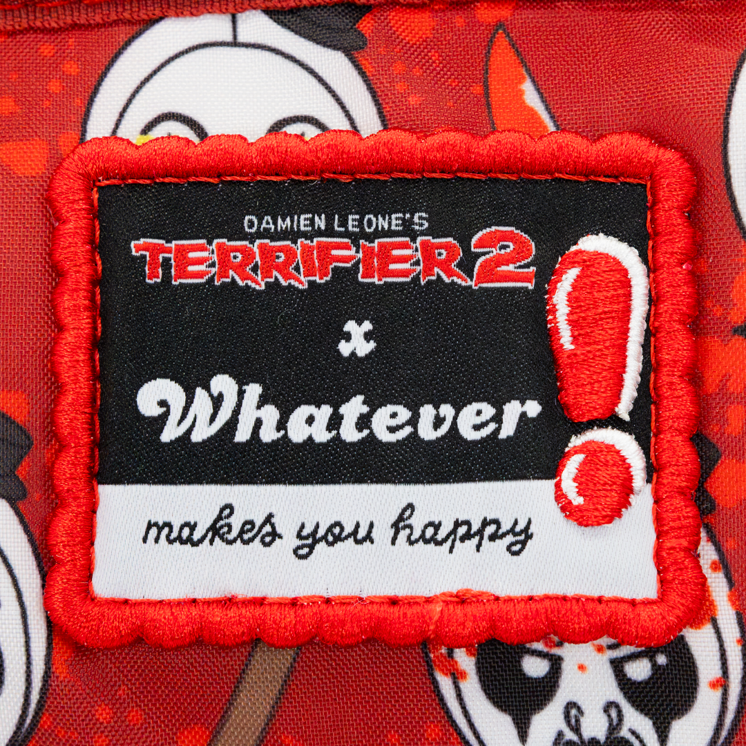Close-up of a rectangular embroidered patch with a scalloped red border, featuring a black center with the text 'DAMien LEONE'S TERRIFIER 2 x Whatever makes you happy' and a red exclamation mark, attached to red printed fabric with cartoon faces.