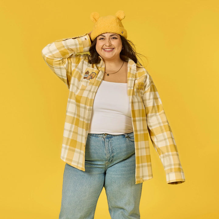 Person wearing a yellow plaid shirt, white top, and jeans against a yellow background