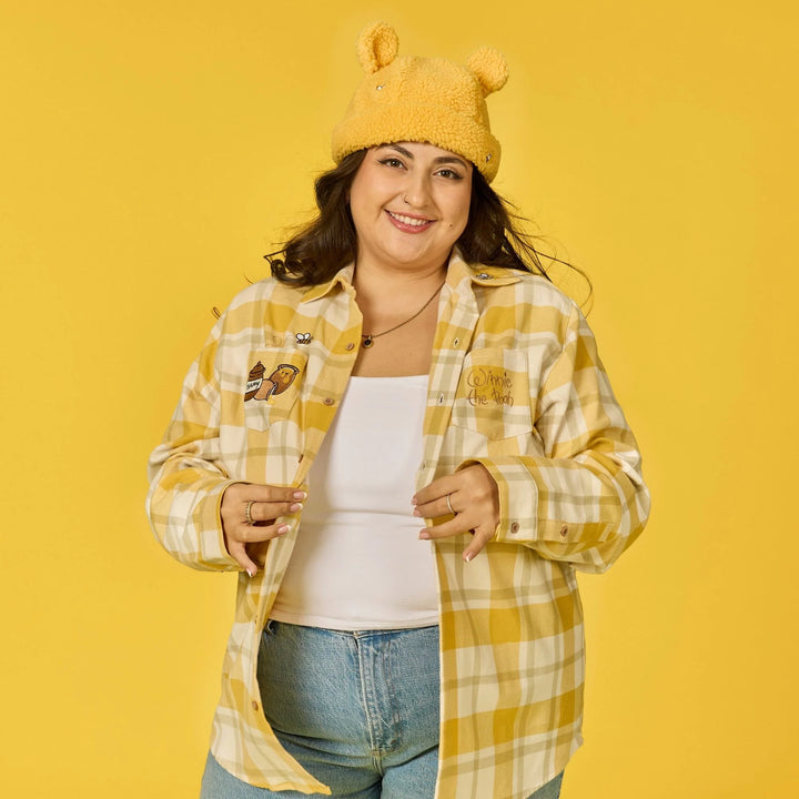 Person wearing a yellow plaid shirt, white top, and jeans with a yellow hat on a yellow background