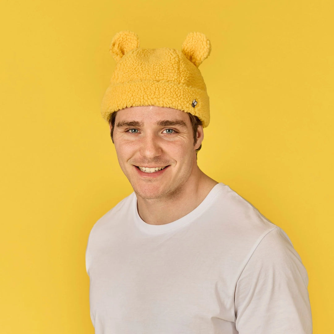 Person wearing a yellow knitted hat with bear ears against a yellow background