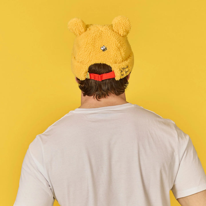 Person wearing a yellow fuzzy beanie with bear ears on a yellow background